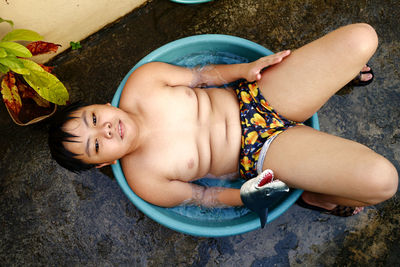 Asian boy cooling down in a water basin and a hose as a makeshift shower to beat the summer heat.