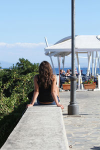 Rear view of woman sitting by trees against sky