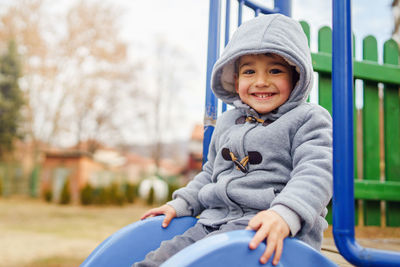 Portrait of smiling boy sitting on slide at playground