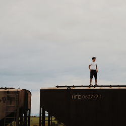 Man standing on railing against sky