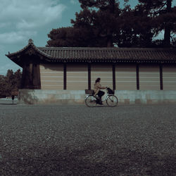 Man riding bicycle by building against sky
