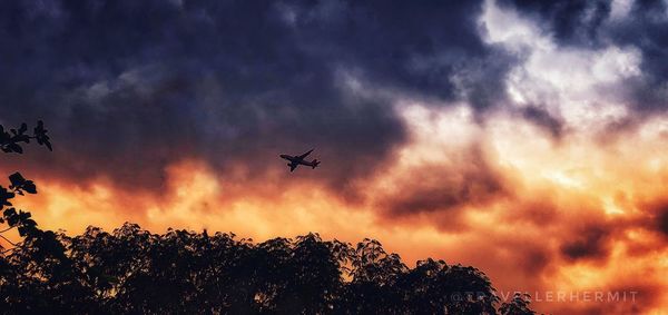 Low angle view of silhouette airplane flying against sky during sunset