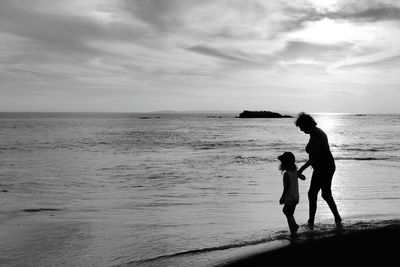 Silhouette mother with daughter on beach against sky