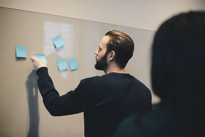 Rear view of businessman explaining plan on adhesive notes to female colleague in office