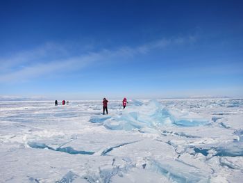 People walking on snow covered landscape against blue sky