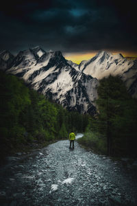 Rear view of man walking on dirt footpath leading towards snowcapped mountains at night