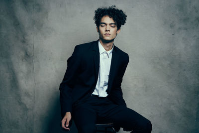 Portrait of young man sitting against wall