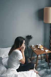 Woman blowing nose while sitting on bed at home