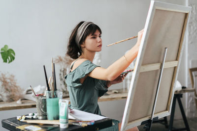 Side view of woman painting on canvas at art studio