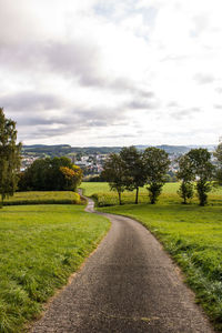 Road amidst trees on field against sky