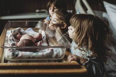Three siblings looking at newborn brother in hospital bassinet
