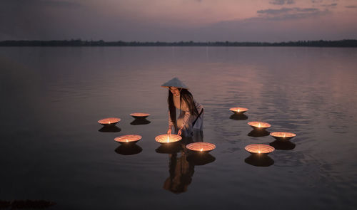 Woman by illuminated diyas in lake