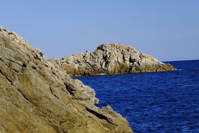 Rock formations by sea against clear blue sky