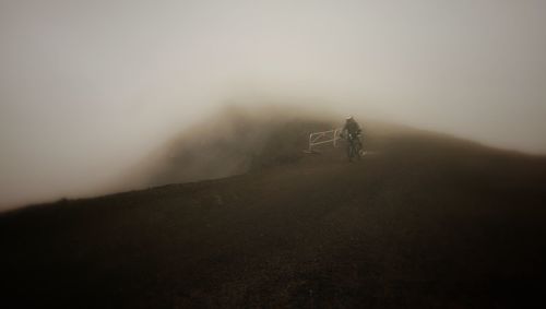 Man riding motorcycle on field against sky during foggy weather