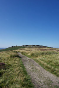 Road amidst field against clear blue sky