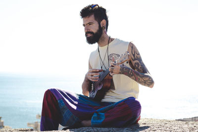 Young man sitting on shore at beach against sky