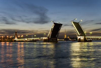 Illuminated city by river against sky at dusk