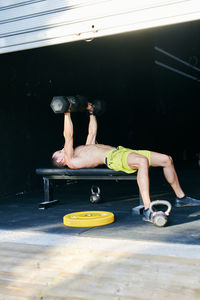 Shirtless fit young man working out in a garage with dumbells