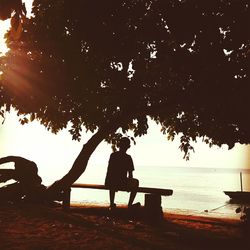 Silhouette men sitting on beach against sky