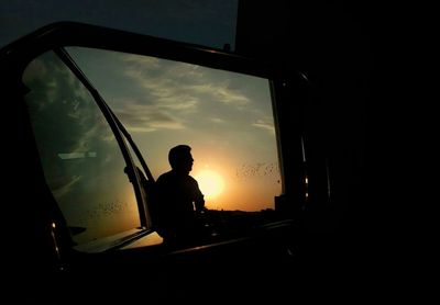 Silhouette of man in mirror against sky during sunset