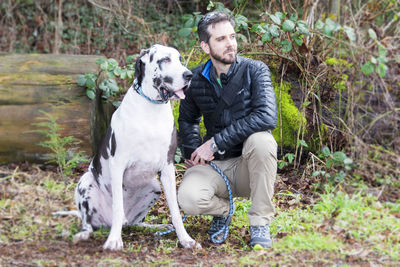 Handsome man crouching by great dane in forest