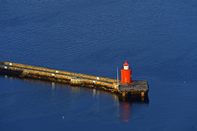 Lighthouse by sea and buildings against blue sky