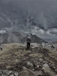 Full length of male hiker walking on rocky mountain against storm clouds