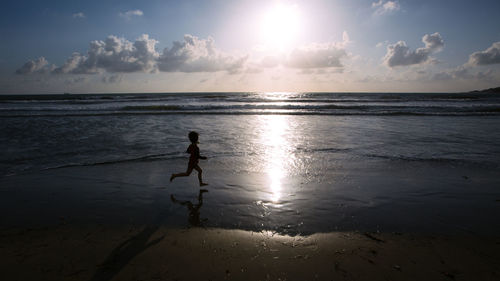 Side view silhouette of boy running on beach against sky