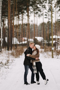 A happy couple in love in winter clothes hugging together walking in a snowy forest on an weekend