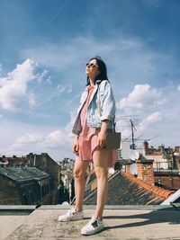 Full length of young woman standing against sky in city
