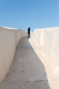 Rear view of man walking on white walkway against clear blue sky