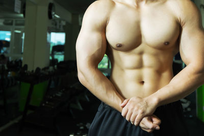 Midsection of shirtless man flexing muscles in gym