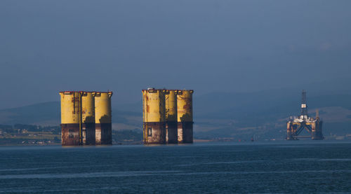 Illuminated buildings in front of sea against clear blue sky
