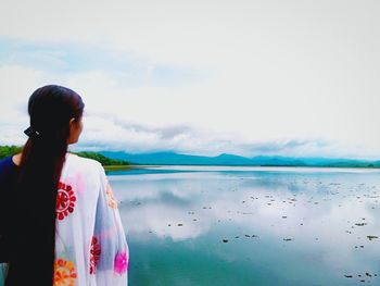 Rear view of woman standing by sea against sky