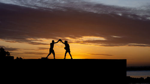 Silhouette of two men doing boxing training on beach against sky during sunset