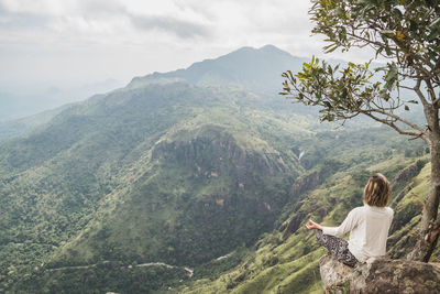 Woman sitting on mountain against sky