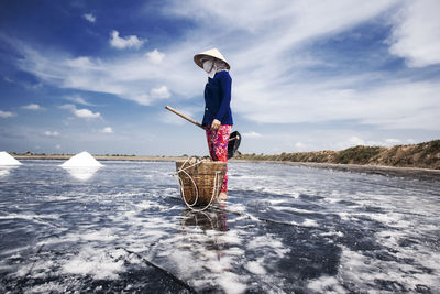 Woman standing by basket against sky in water