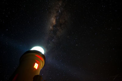 Low angle view of illuminated lighthouse against star field