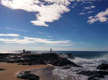 Silhouette men on rock formation fishing in sea