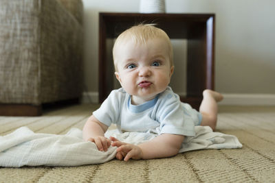 Portrait of cute playful baby boy making face while lying on carpet at home