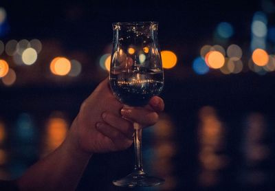 Cropped hand holding wineglass outdoors at night