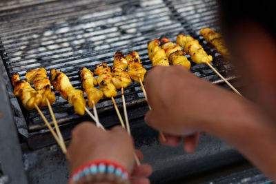 Cropped hands of person making satay on barbeque grill