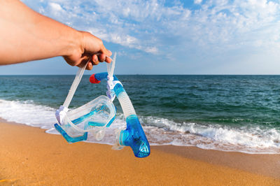 Midsection of woman holding water bottle at beach against sky