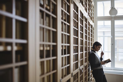 Thoughtful female lawyer researching while leaning on shelf in library