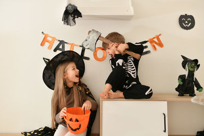 Children in skeleton and witch costume laughing at home