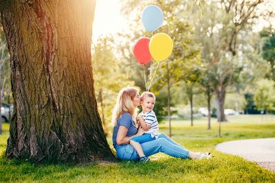 Woman kissing son with balloons against tree at park