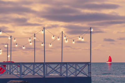 Romantic pier at sunset with glowing bulbs, side view. yacht with red sail is on the horizon.
