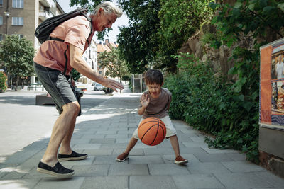Grandfather playing basketball with grandson on sidewalk