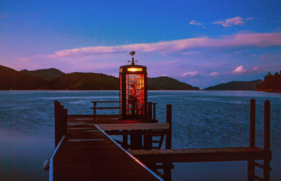 Man in telephone booth on pier by sea during sunset