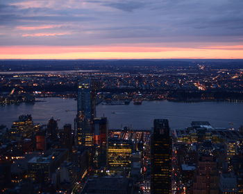 Aerial view of river amidst illuminated cityscape during sunset